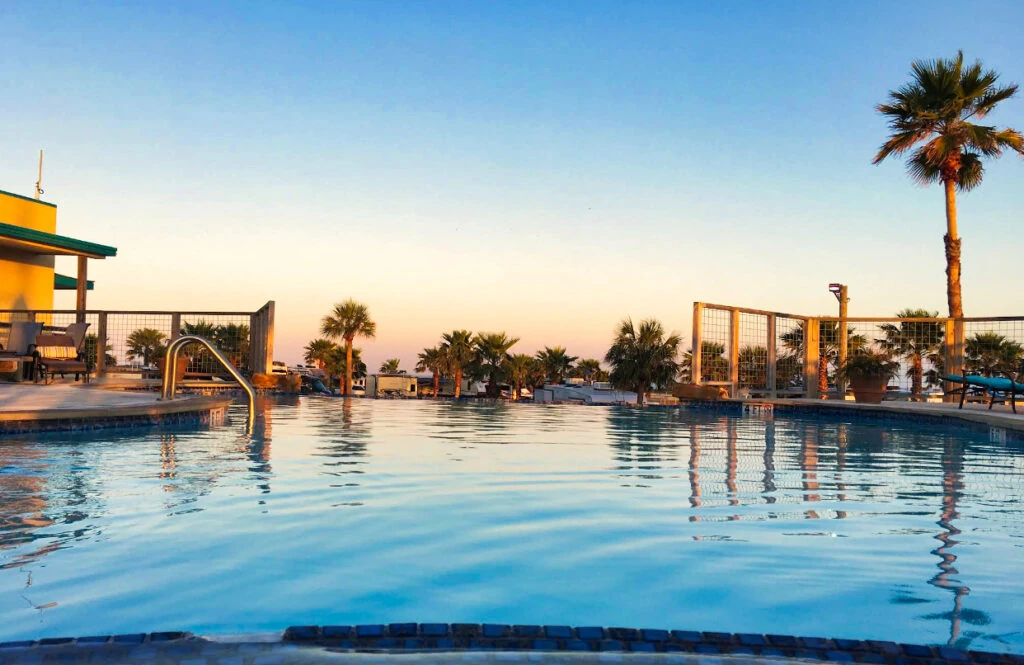 Calm pool water reflecting palms and the warm evening sky