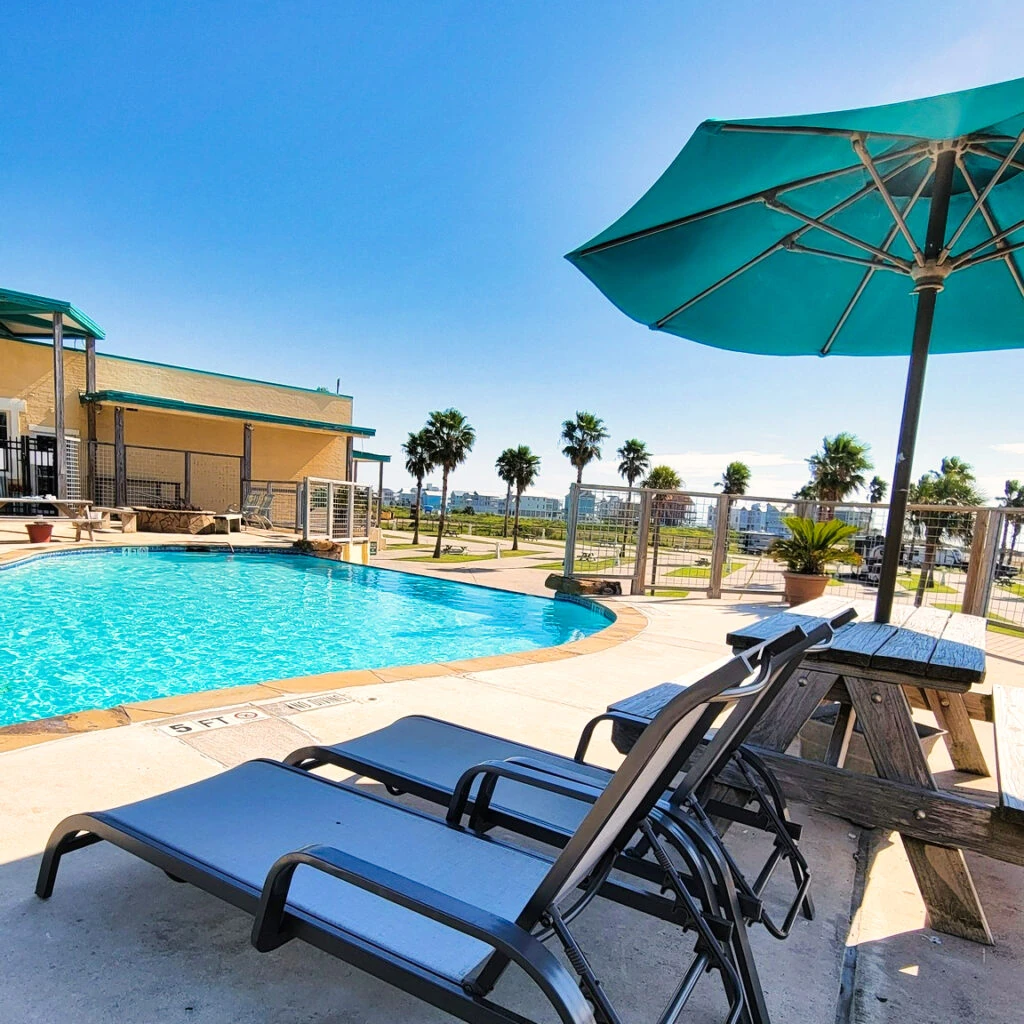 Poolside lounge chairs beside a turquoise umbrella and the resort pool